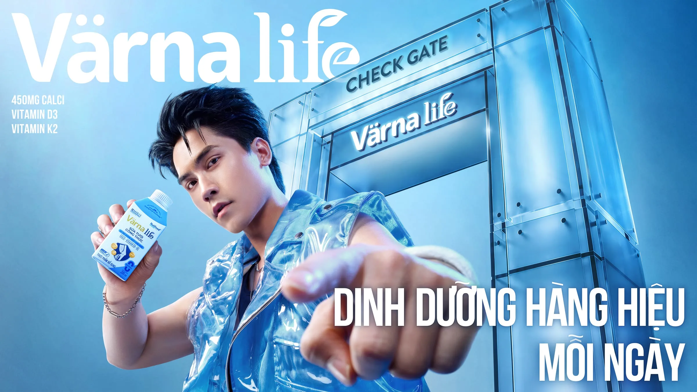 Nam diễn viên mặc áo khoác xanh nhạt, tay cầm hộp sữa Värna trước cổng kiểm soát với dòng chữ lớn trên nền xanh.