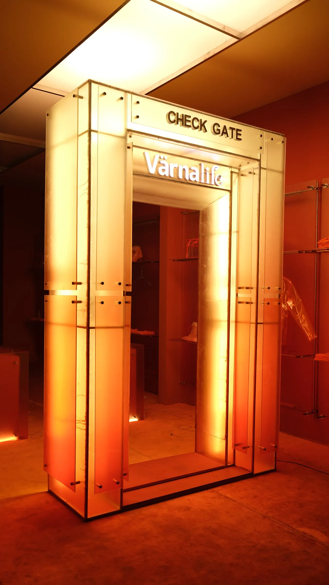 Cổng kiểm soát với đèn neon màu cam rực sáng, trên đó ghi chữ CHECK GATE và logo VärnaLife.
